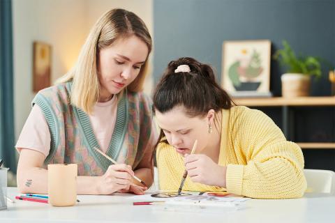 Caregiver helping woman paint.